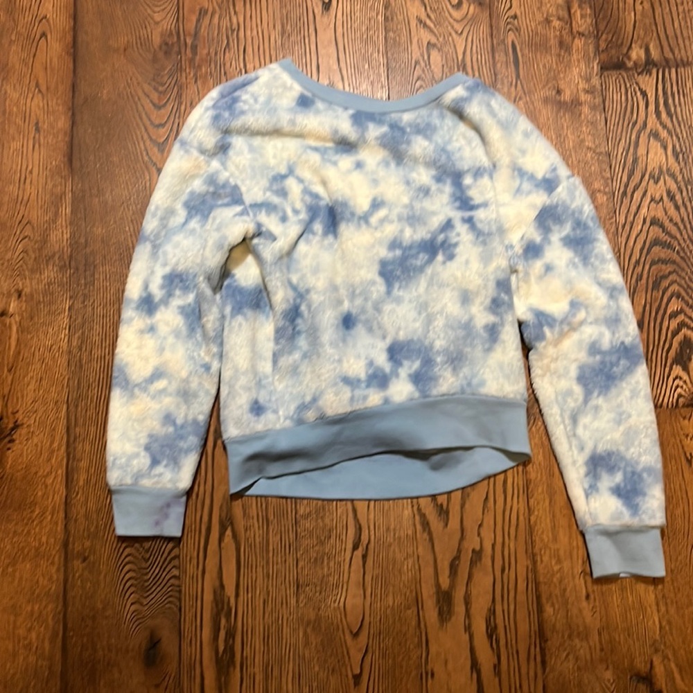 A tie-dye,fluffy blue and white sweater with a bit of a purple stain on the hand
